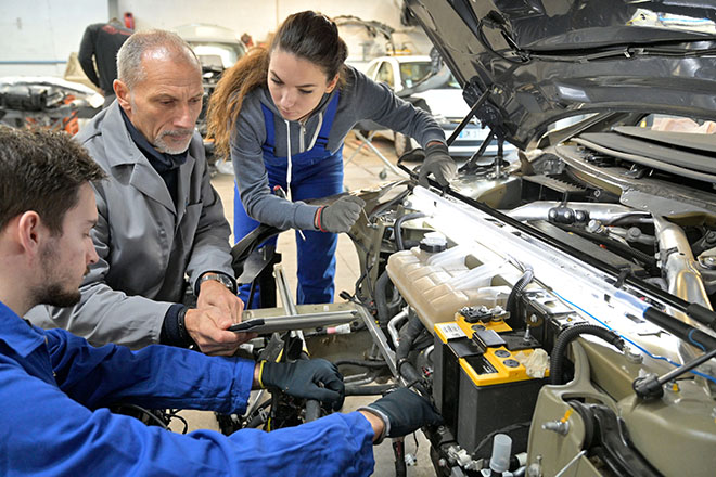 Una joven, un adulto de mediana edad y un joven, trabajan en la revisión de un vehículo